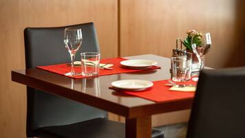 Una mesa de comedor con un mantel individual rojo, copas transparentes, un plato blanco y una pequeña planta en maceta.