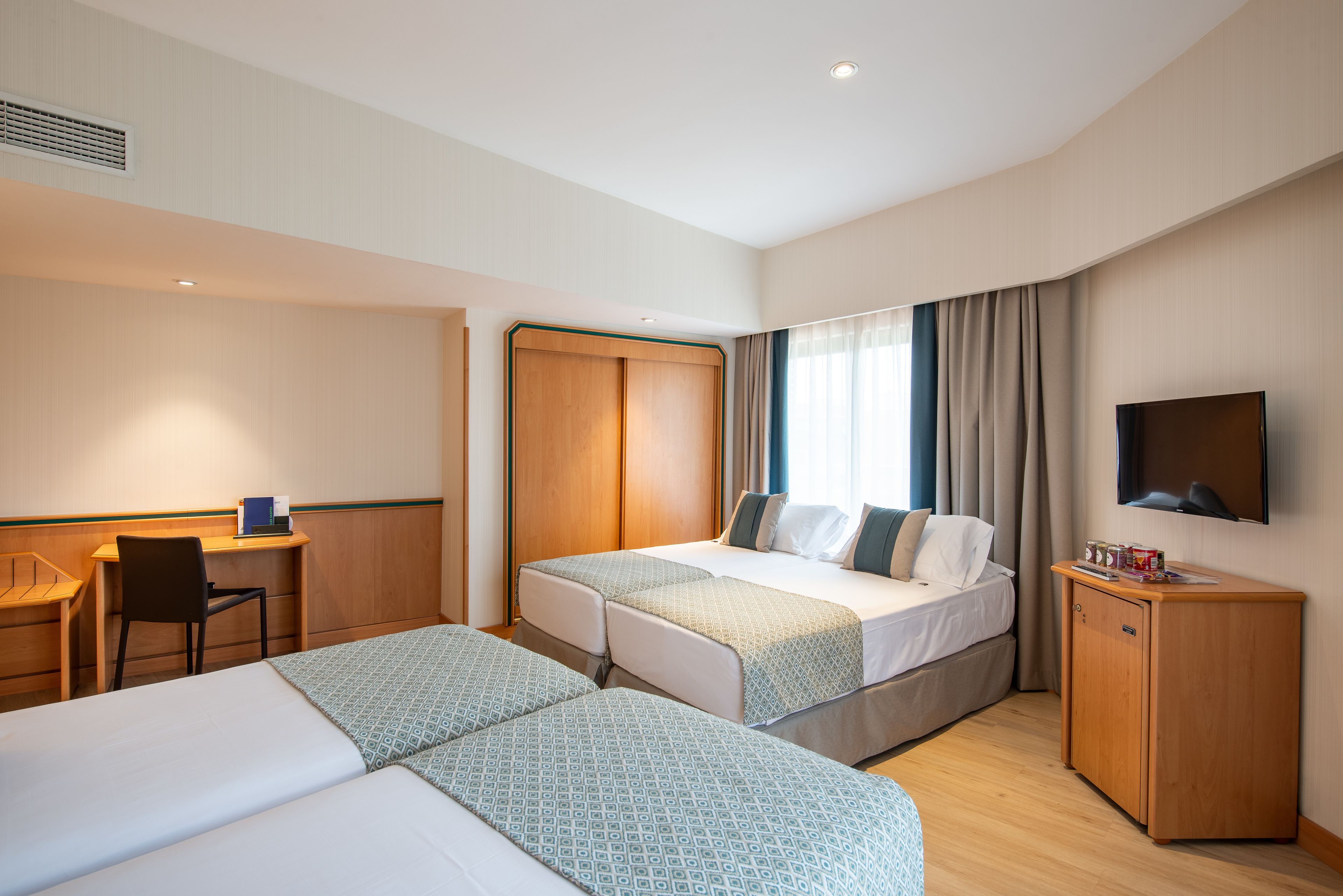 Une chambre d’hôtel avec deux lits, un bureau, une chaise, une télévision et une armoire.
