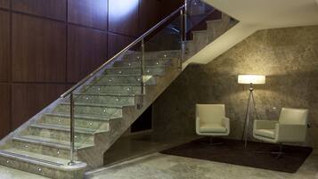 Un interior moderno con una escalera de mármol, dos sillas blancas, una lámpara de pie y una pared con textura.