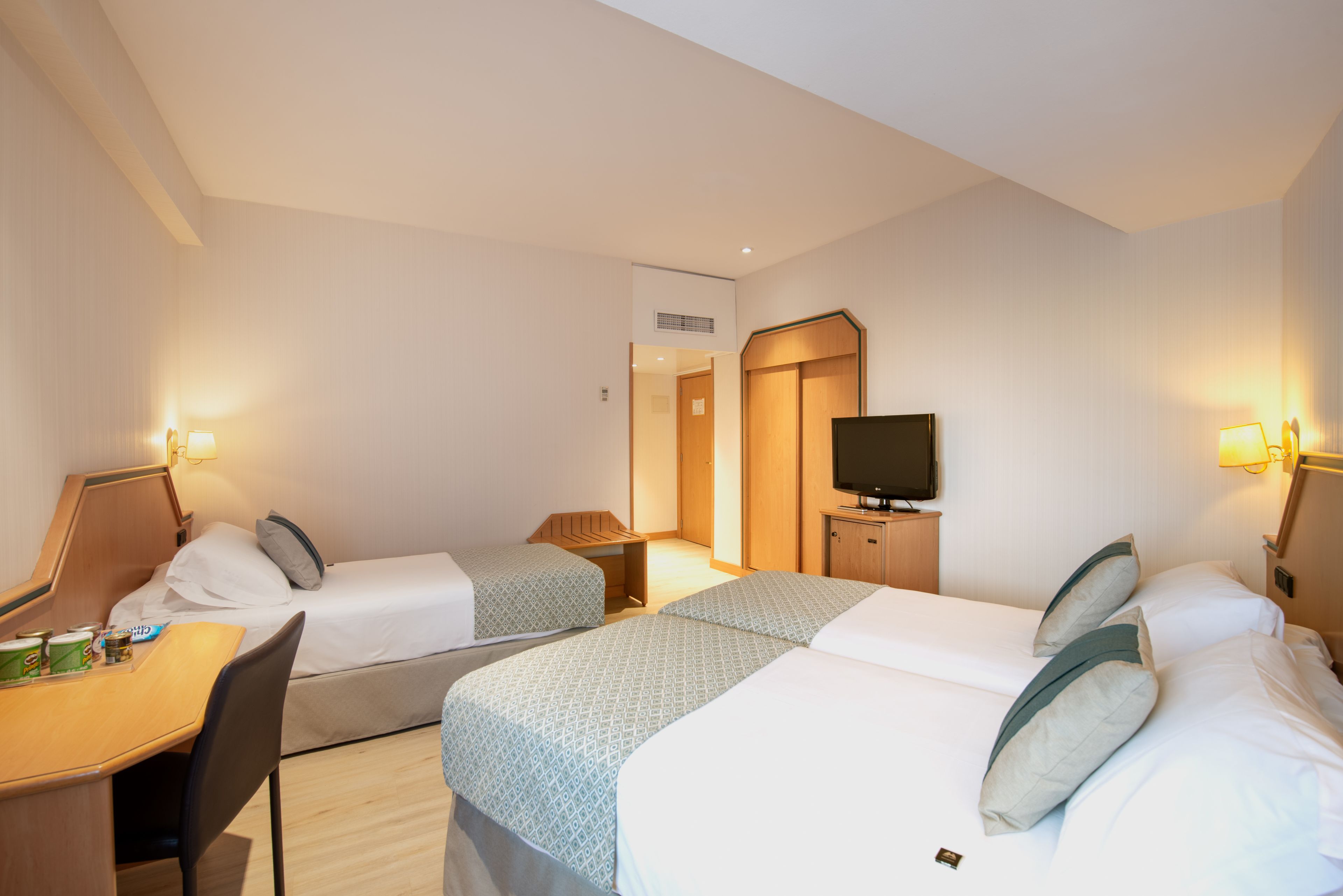 Une chambre d’hôtel avec deux lits, un bureau, une chaise, une télévision et une petite table sur laquelle se trouvent divers objets.