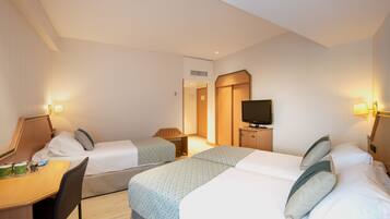 Une chambre d’hôtel avec deux lits, un bureau, une chaise, une télévision et une petite table sur laquelle se trouvent divers objets.