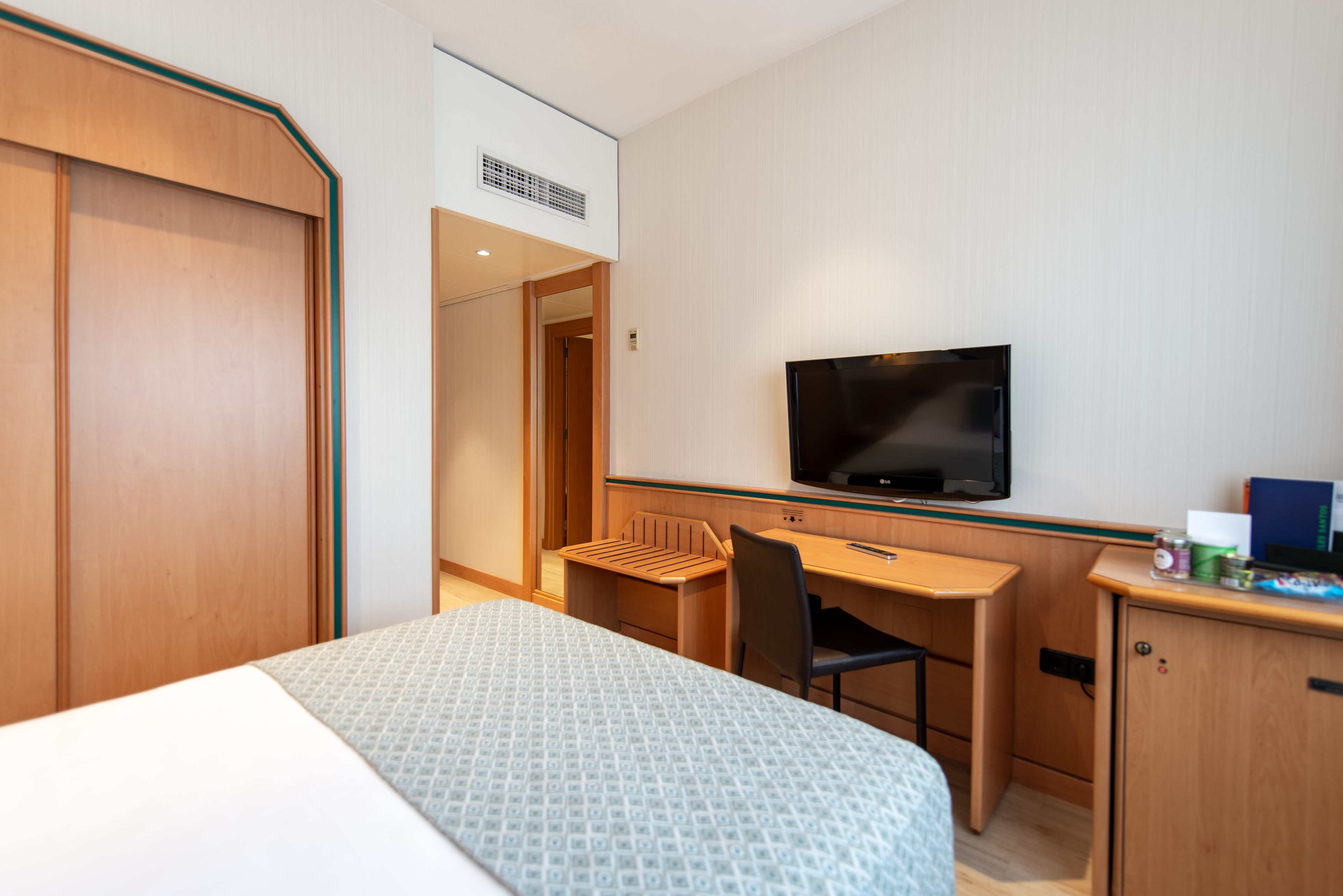 Habitación de hotel con cama, escritorio, silla, televisor y armario.