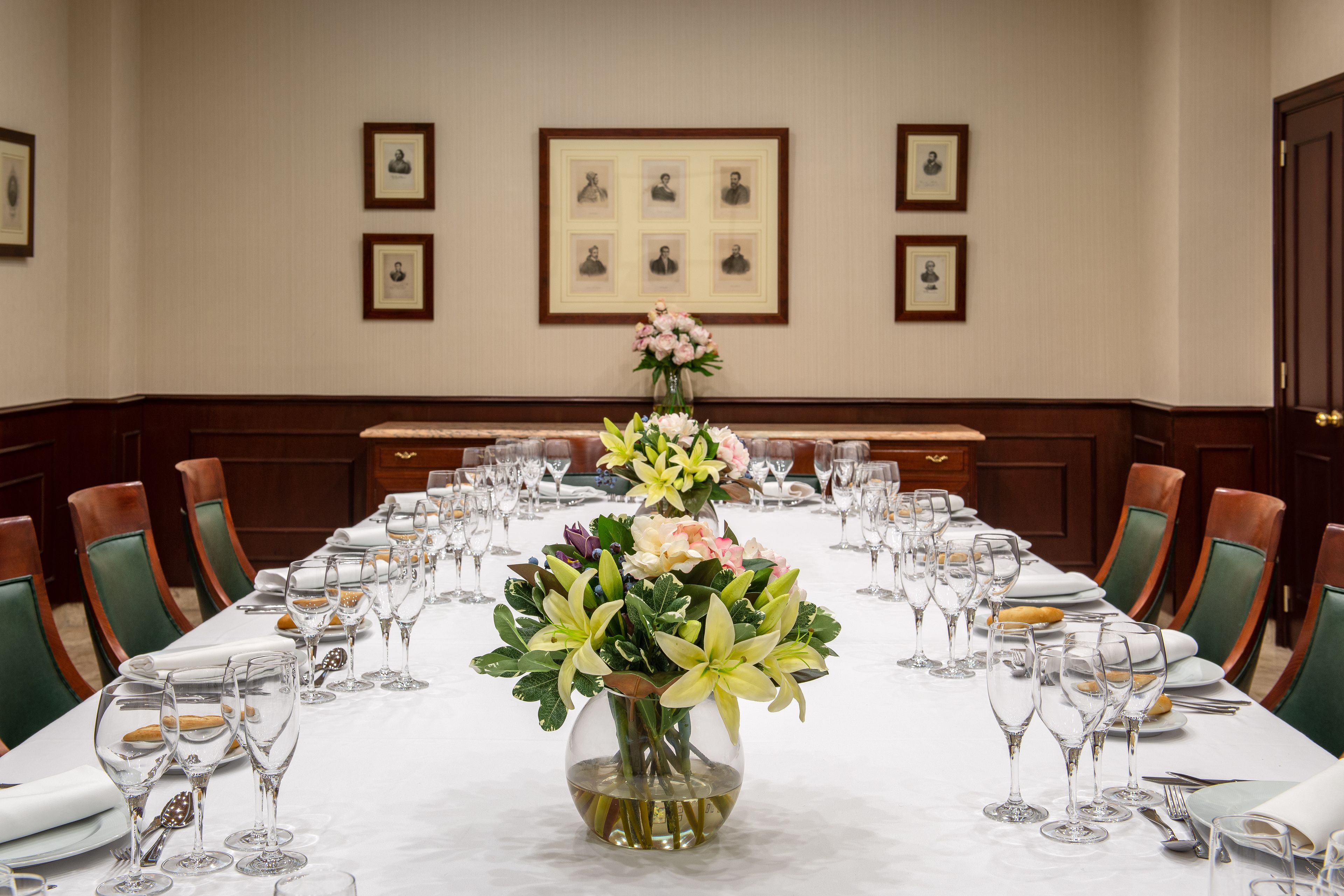 Una larga mesa de comedor dispuesta con sillas, un jarrón con flores y cuadros en la pared.