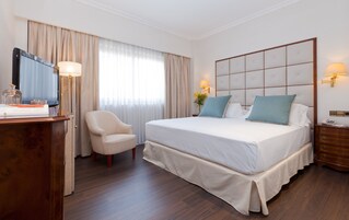 Una habitación de hotel con una cama grande, un escritorio con lámpara, una silla y un televisor.