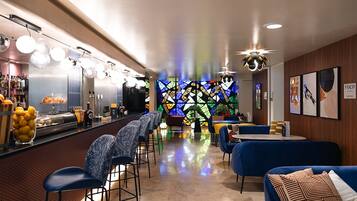 A bar area with stools, a counter with beverages, and a colorful stained glass wall.