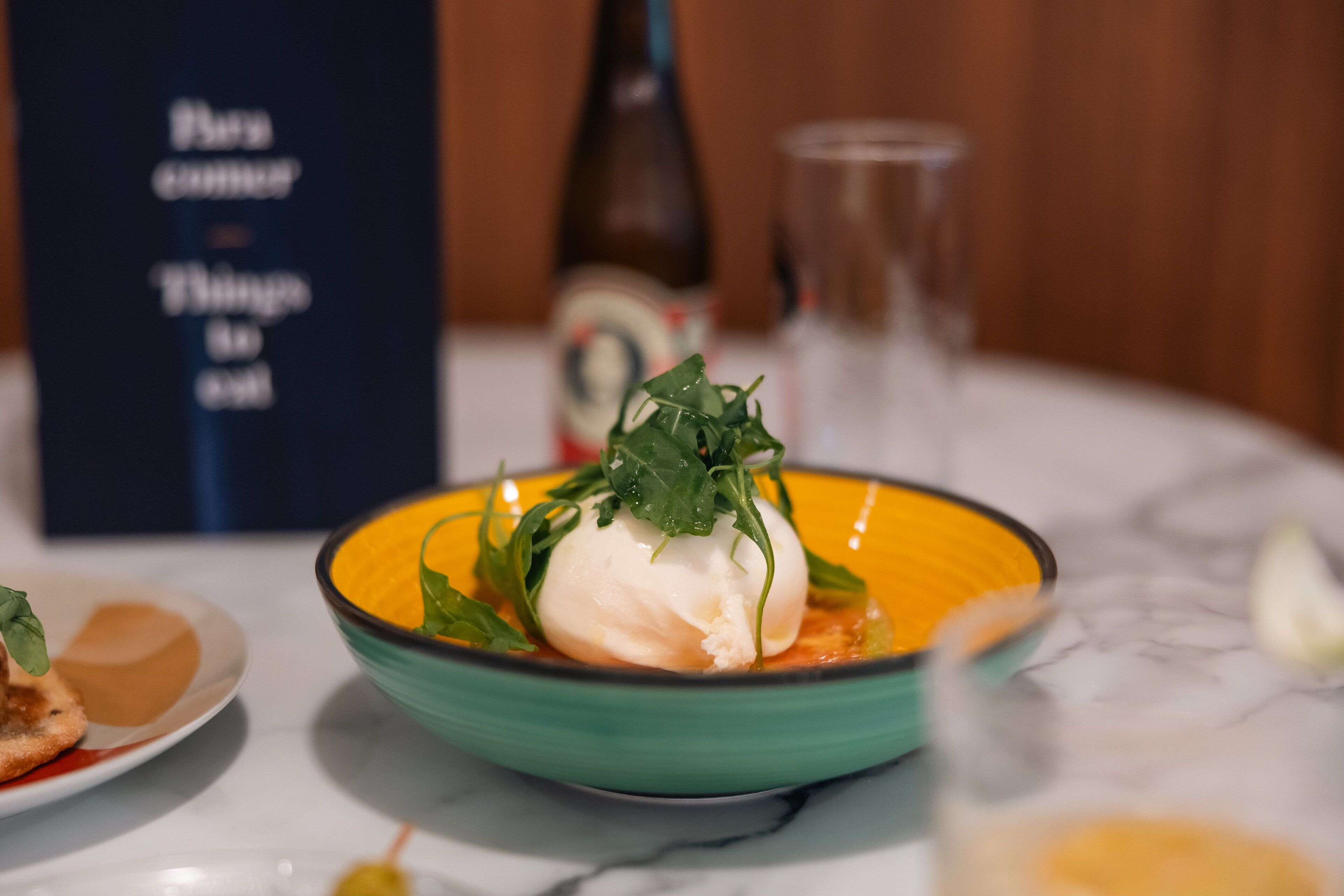 A table setting with a bowl of food, a bottle, and a menu.