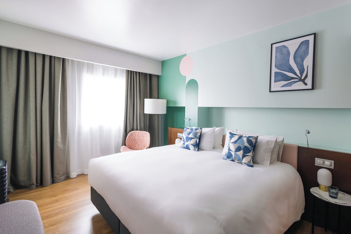 Una camera d'albergo con un letto grande, una sedia, una lampada e un quadro appeso al muro.