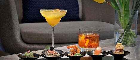 Una mesa con una copa de martini, una limonada helada y diversos aperitivos.