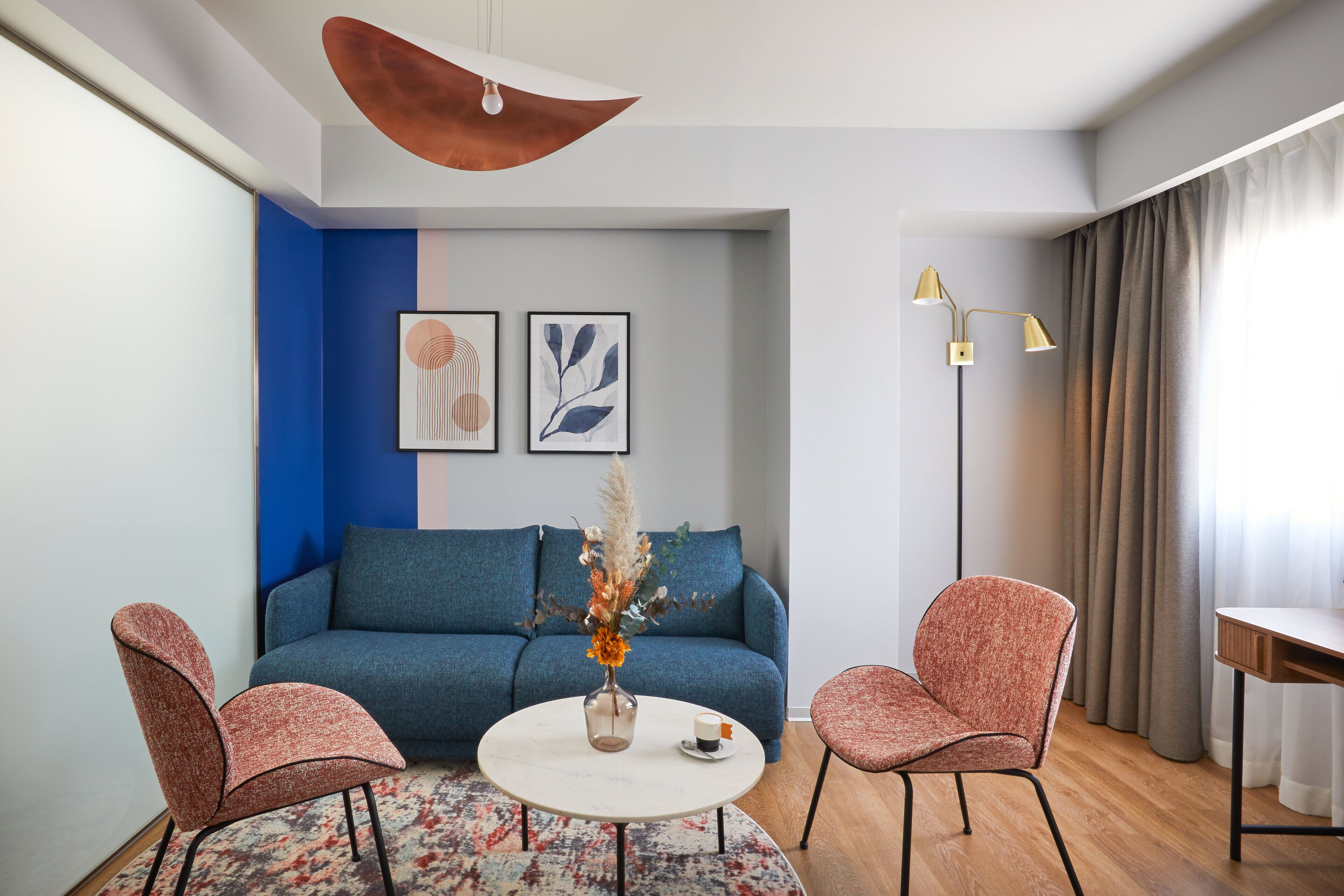 Ein modernes Wohnzimmer mit einem blauen Sofa, zwei Sesseln, einem Couchtisch und einer Stehlampe.