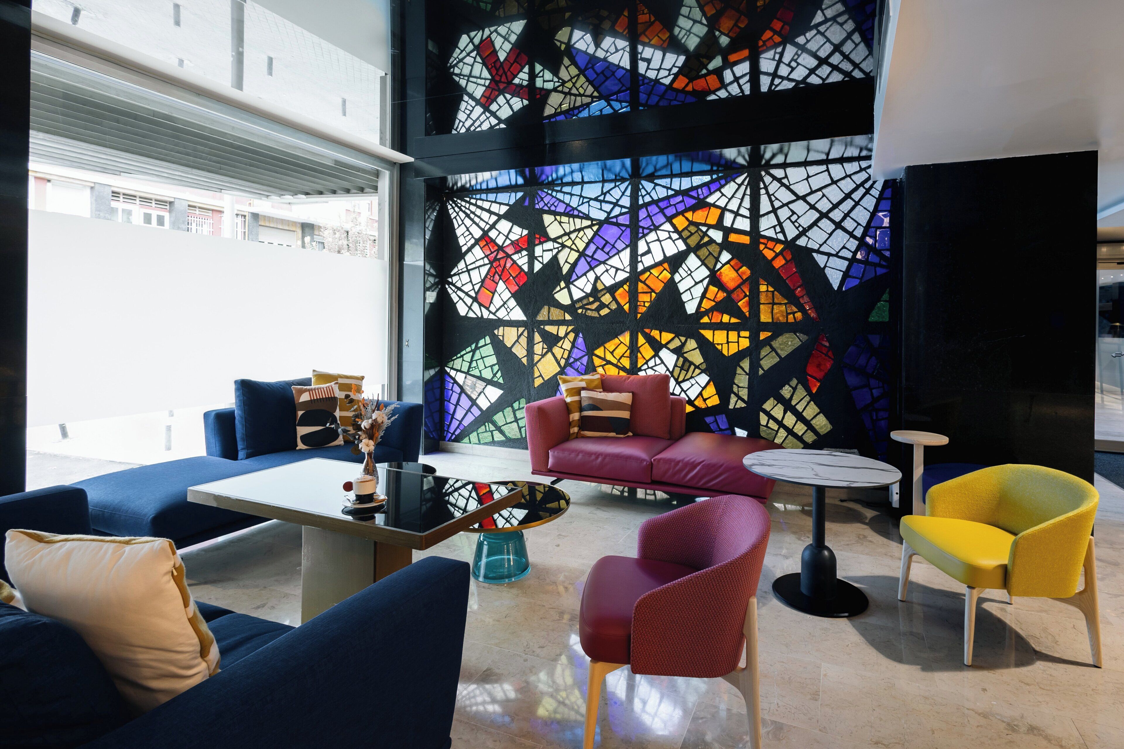 Un área de descanso moderna con sofás azules, un sofá rojo y un sillón amarillo, junto a una mesa de centro.