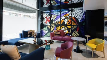 Un área de descanso moderna con sofás azules, un sofá rojo y un sillón amarillo, junto a una mesa de centro.