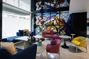 Un área de descanso moderna con sofás azules, un sofá rojo y un sillón amarillo, junto a una mesa de centro.