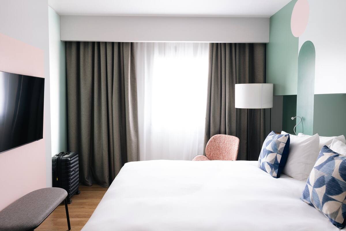 Ein Hotelzimmer mit Bett, Sitzbank, Stuhl, Fernseher und Lampe.
