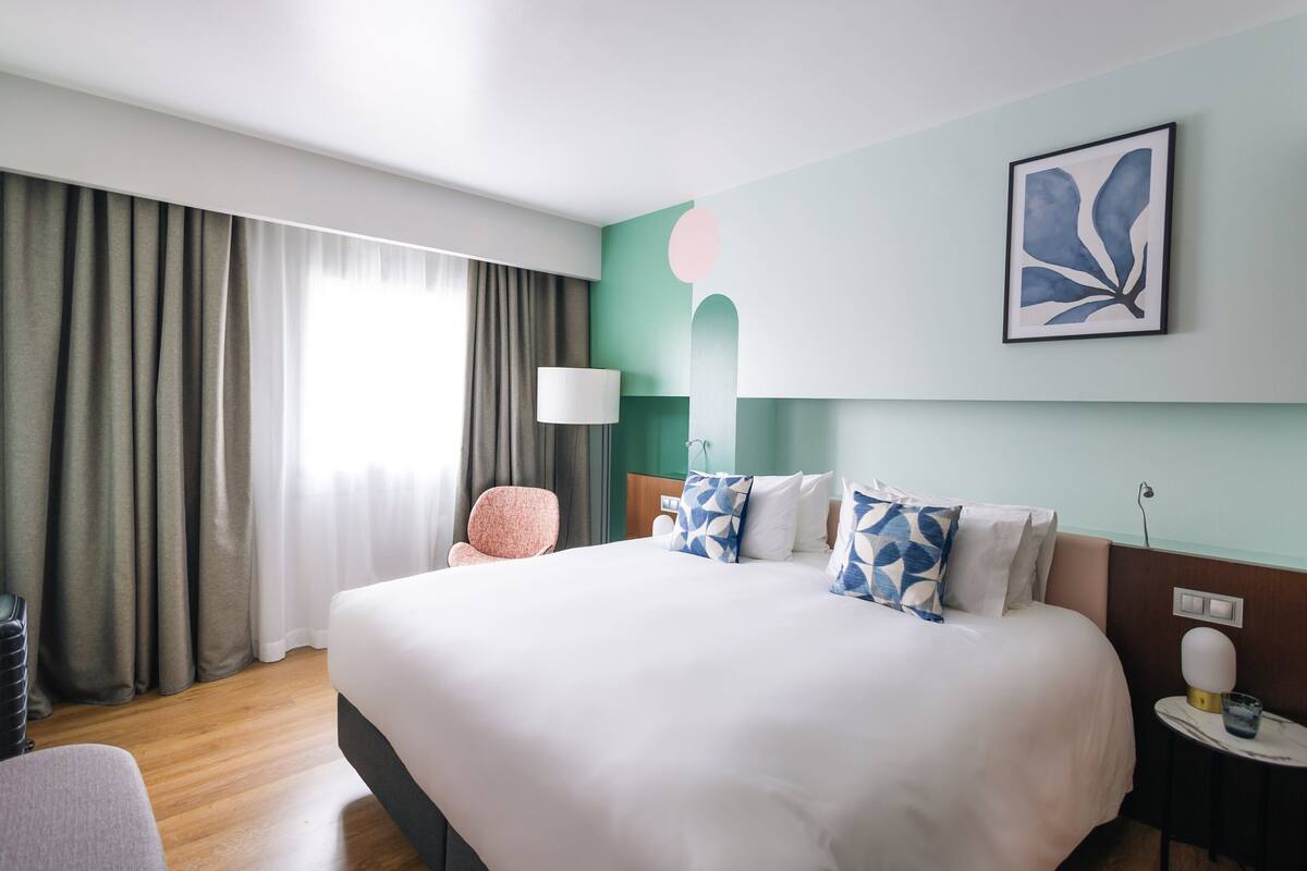 Ein Hotelzimmer mit einem großen Bett, einem Sessel, einer Lampe und einem Wandbild.