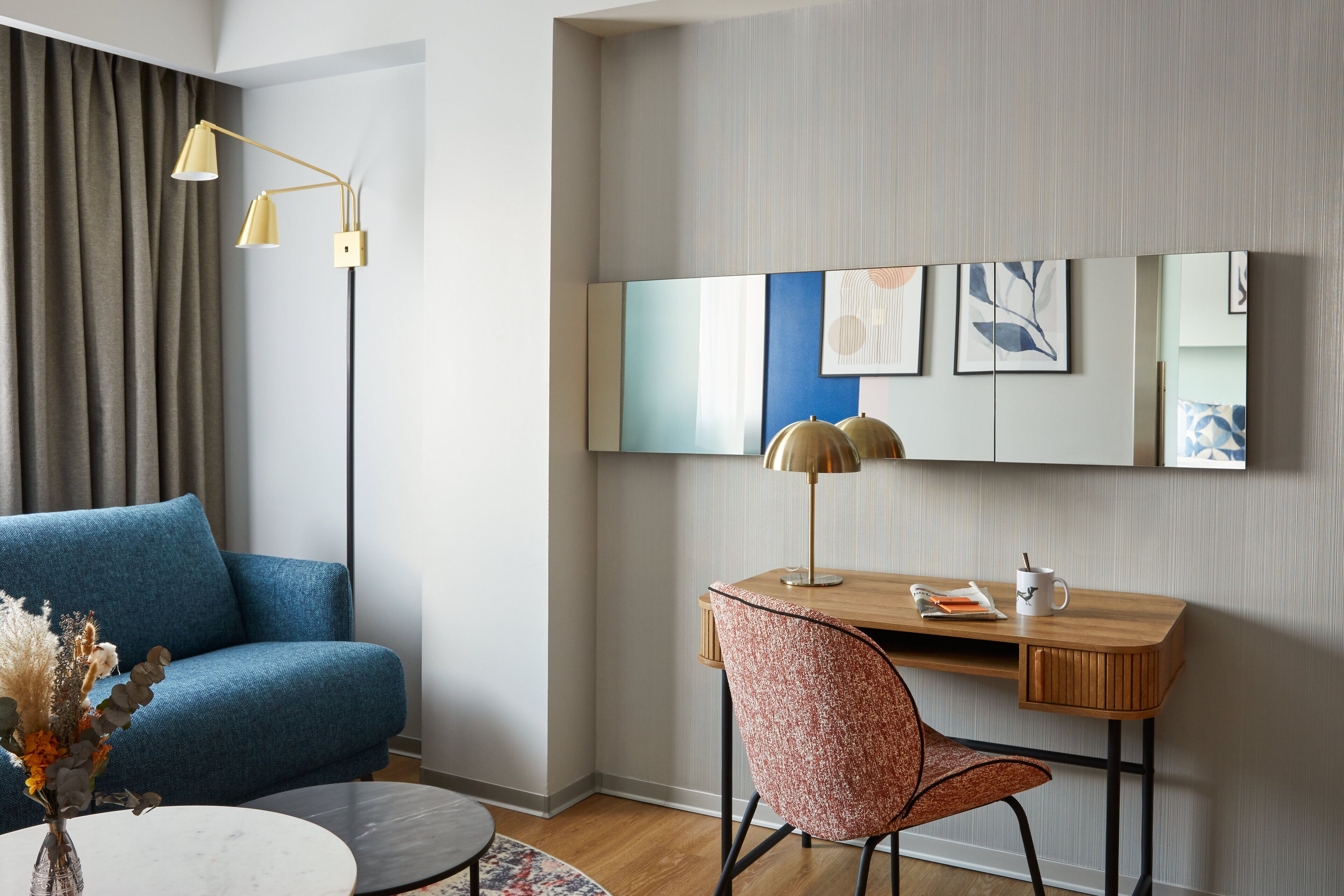 A modern room with a blue sofa, a wooden desk, a chair, a lamp, and artwork on the wall.