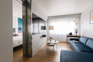 Una habitación de hotel moderna con una cama, un sofá, una mesita y un escritorio con una lámpara.
