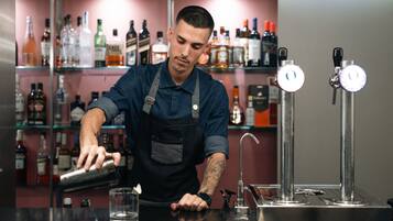 Een barman maakt een drankje klaar achter een bar, met flessen drank op de achtergrond.