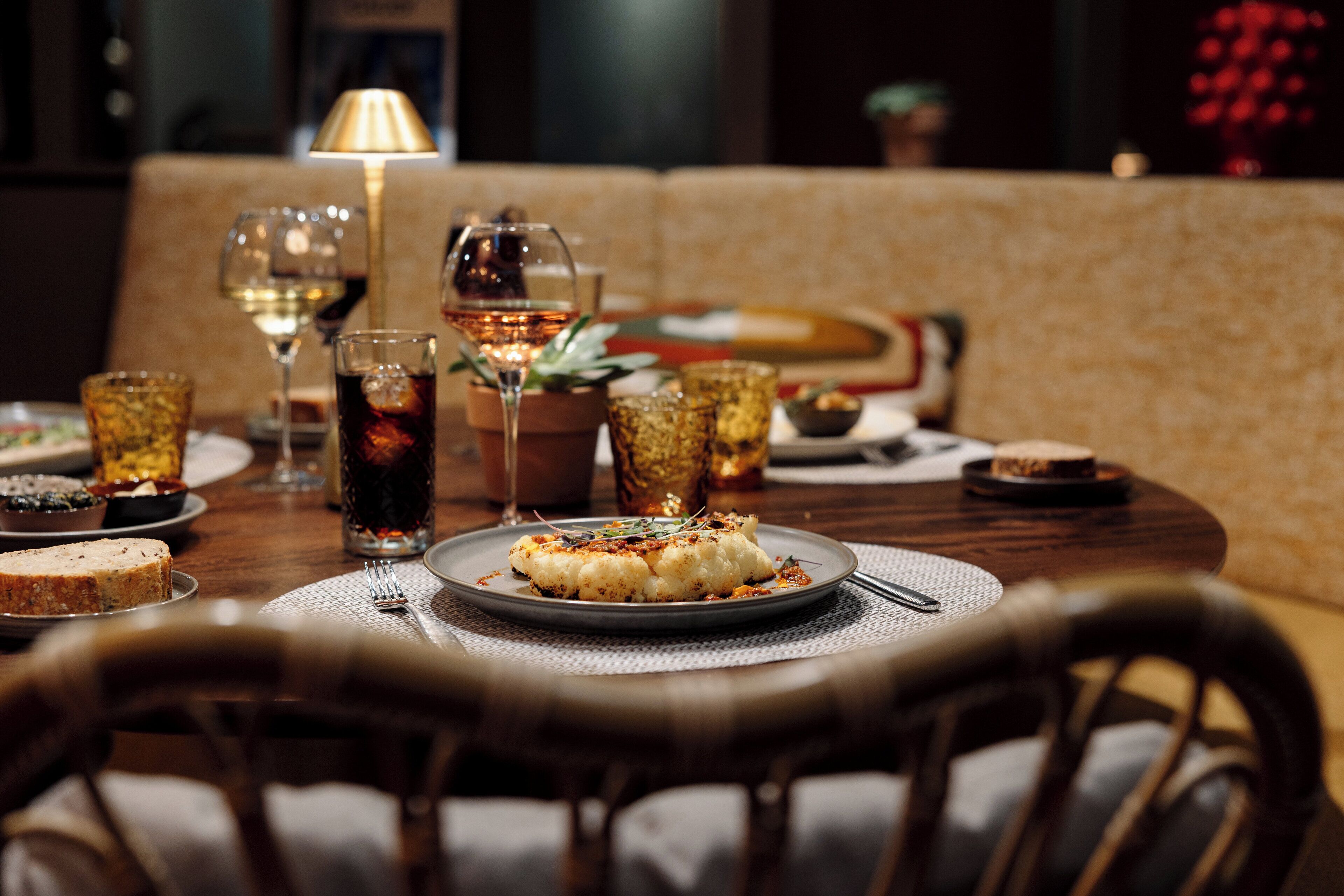 Una mesa de comedor dispuesta con platos de comida, vasos y una vela.