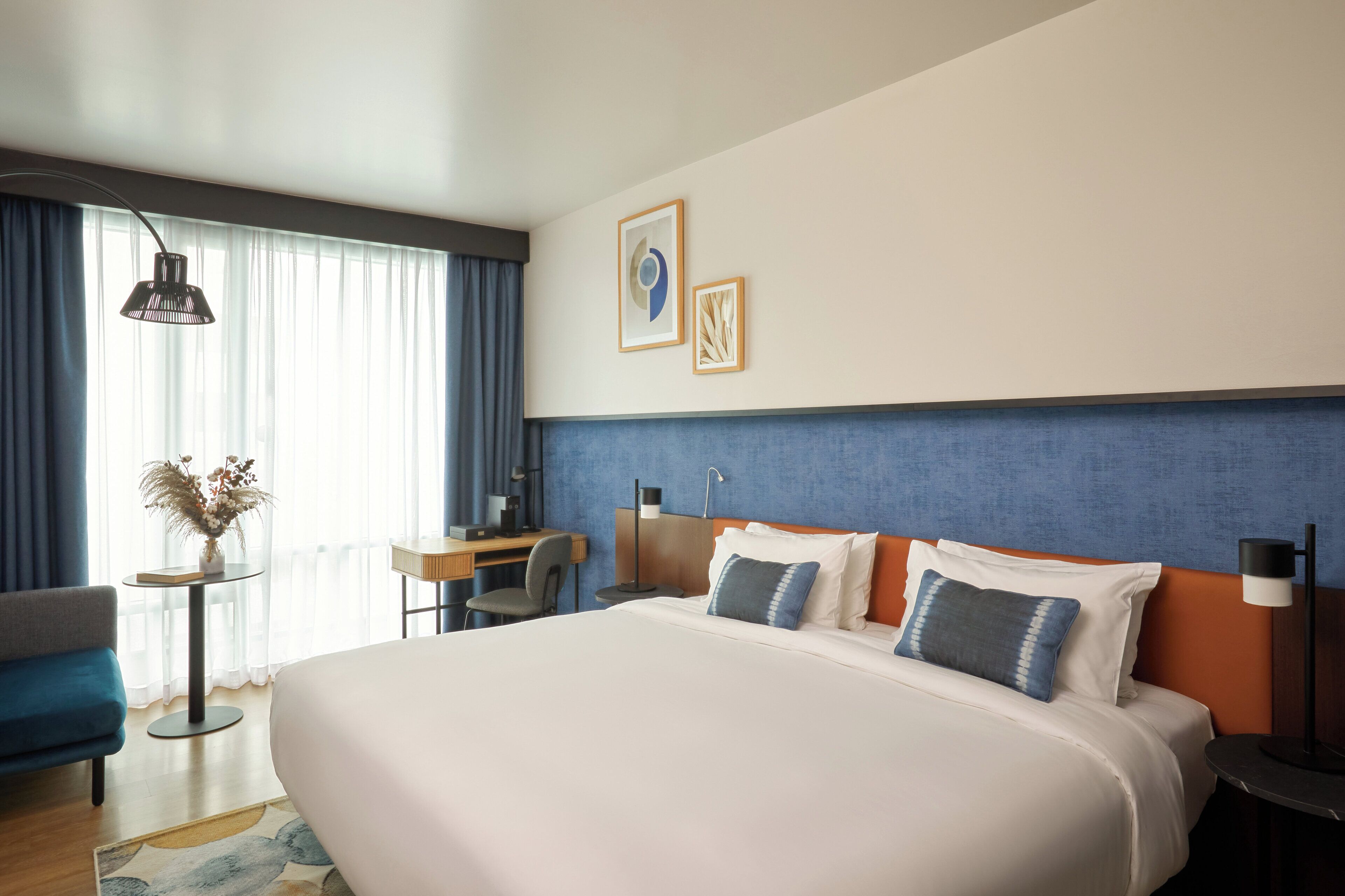 Een hotelkamer met een groot bed, een bureau, een stoel en een kleine tafel met een bloevas.
