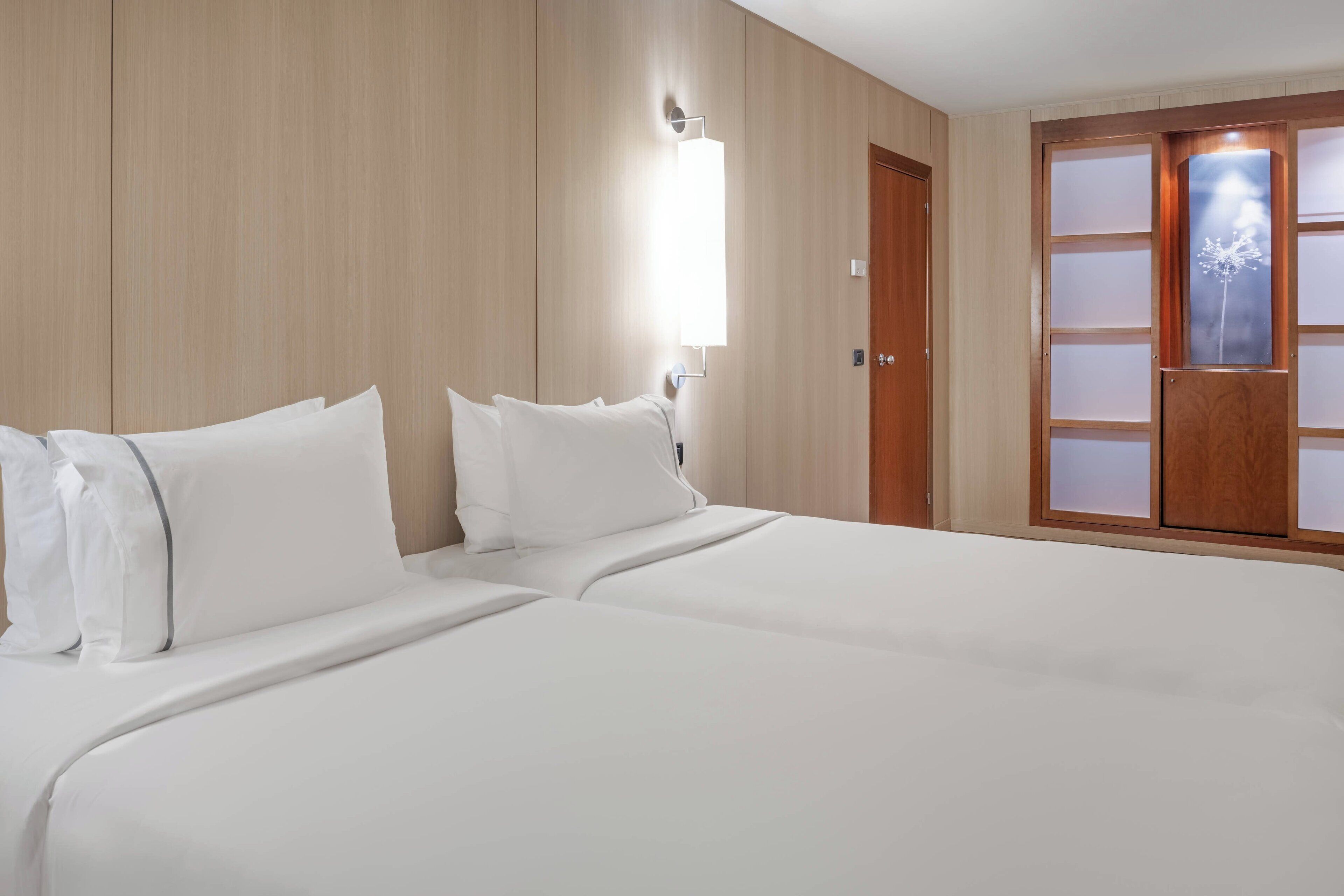 Ein Hotelzimmer mit einem großen Bett, Holzwandverkleidung, einer Holztür mit satinierten Glasscheiben und einer an der Wand montierten Leuchte.