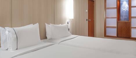 A hotel room with a large bed, wooden panel walls, a wooden door with frosted glass panels, and a wall-mounted light fixture.