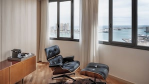 Une chambre moderne dotée d’une grande fenêtre, d’un fauteuil en cuir, d’un petit pouf et d’une armoire en bois.