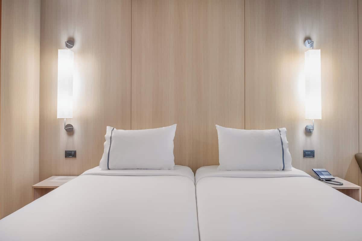 Een tweepersoonskamer met twee bedden, elk voorzien van een kussen en een nachtkastje met een telefoon.