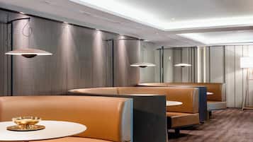 A modern hotel lobby with leather seating, pendant lighting, and a patterned wall.
