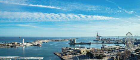A coastal cityscape with a marina, a large Ferris wheel, and a prominent lighthouse.