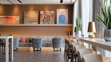 Un moderno vestíbulo de hotel con una zona de estar, una mesa larga y obras de arte en la pared.