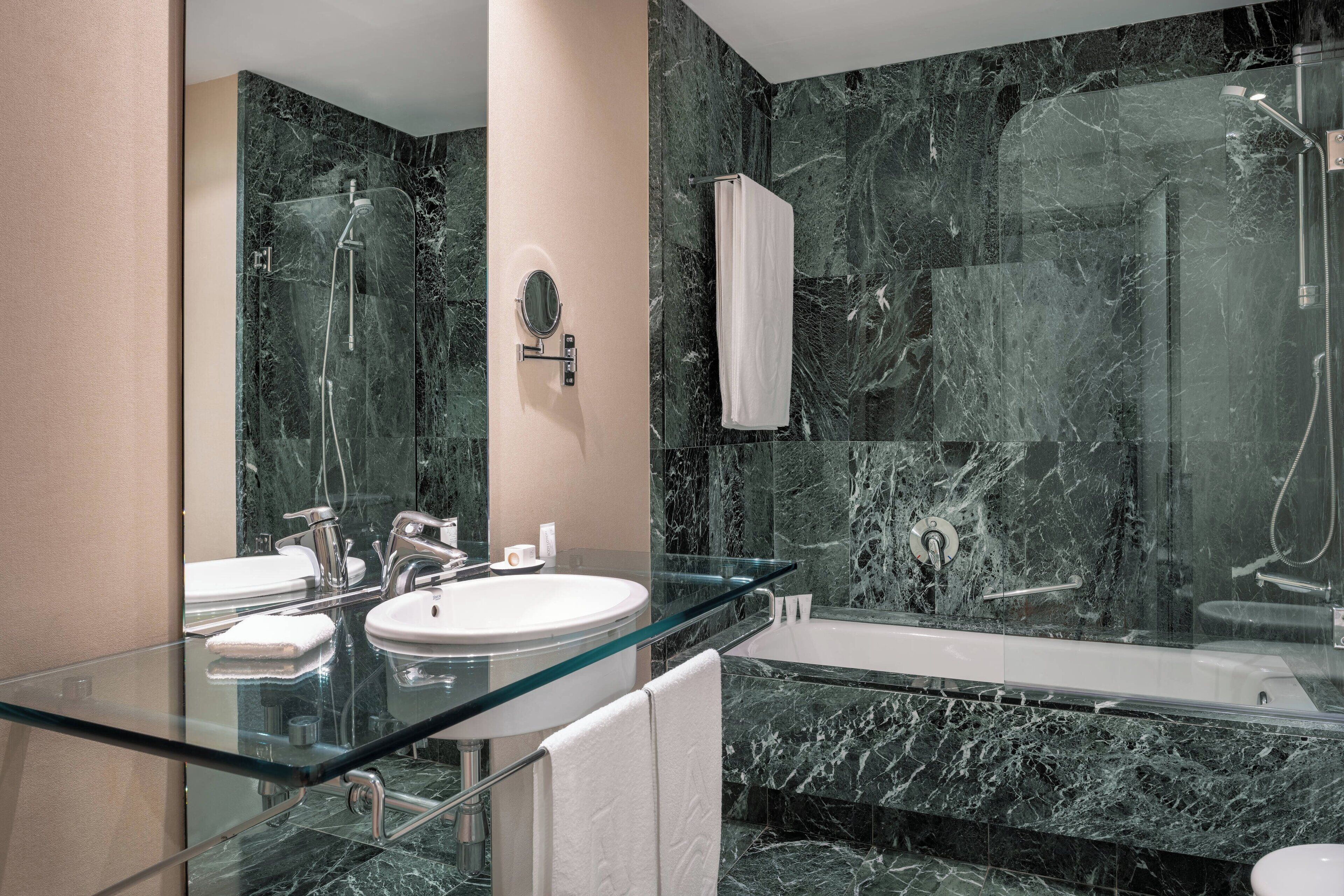 Un baño moderno con dos lavamanos, tocador de vidrio, espejo grande, bañera y cabina de ducha con paredes de vidrio.