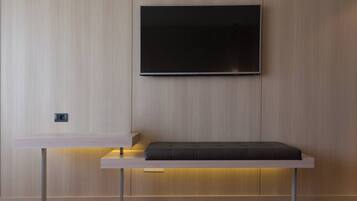 A modern room with a flat-screen TV mounted on the wall, a wooden bench with a cushion, and a built-in shelf below.