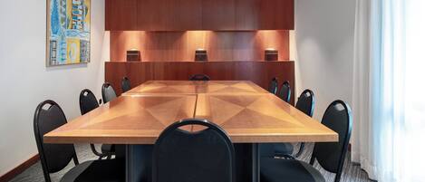 A conference room with a large wooden table, black chairs, recessed lighting, and a painting on the wall.