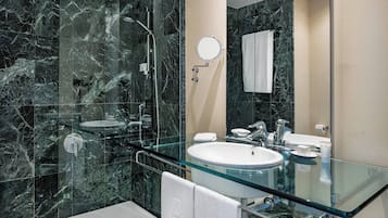 A modern bathroom with a glass-enclosed sink, a handheld showerhead, and a large mirror.