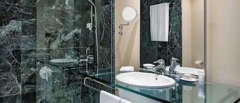 A modern bathroom with a glass-enclosed sink, a handheld showerhead, and a large mirror.