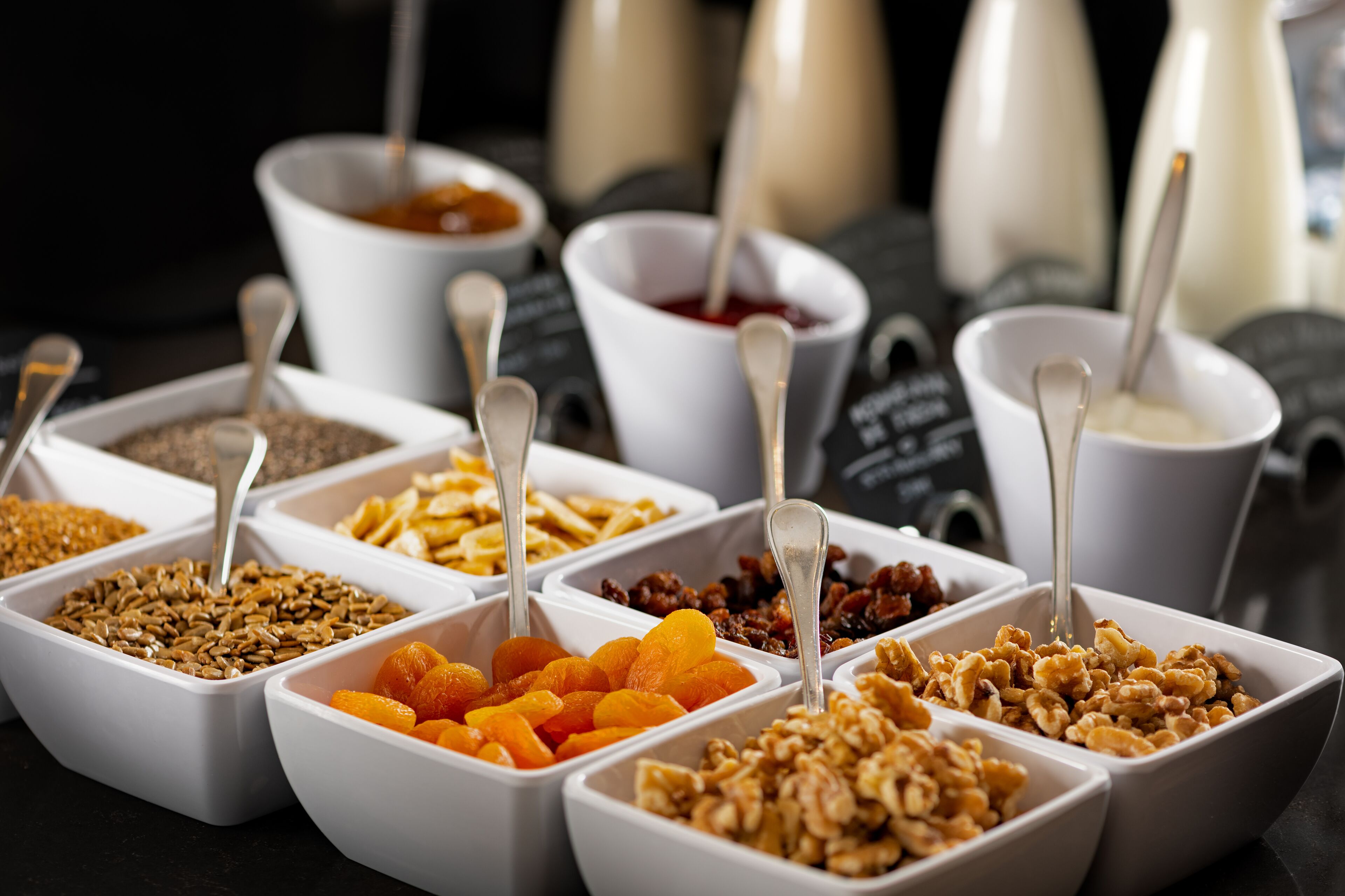 Une variété d’aliments présentés dans des bols blancs, accompagnés de cuillères, et disposés sur une table.