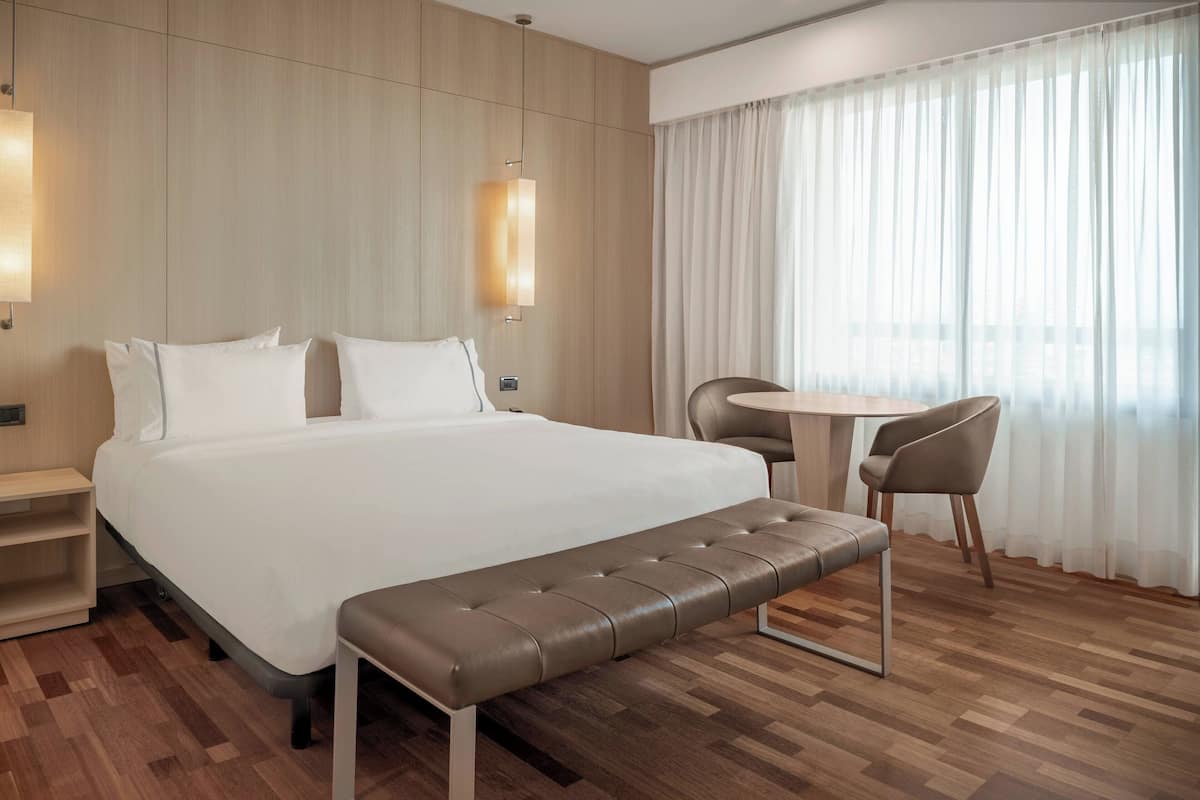 Een moderne hotelkamer met een groot bed, een bankje, een klein tafeltje en een stoel.