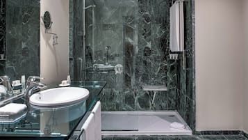 Ein modernes Badezimmer mit einem Waschbecken aus Glas, einer Dusche und Marmorwänden.