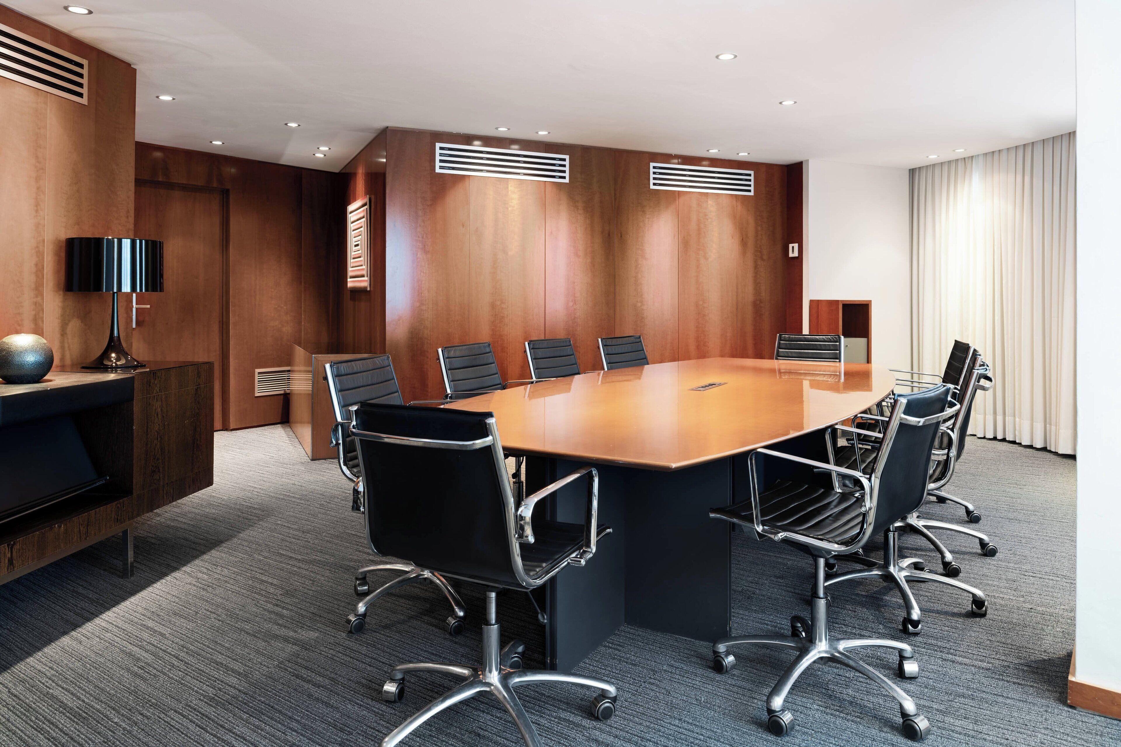 Un salón de conferencias con una amplia mesa de madera, sillas negras y un diseño moderno.