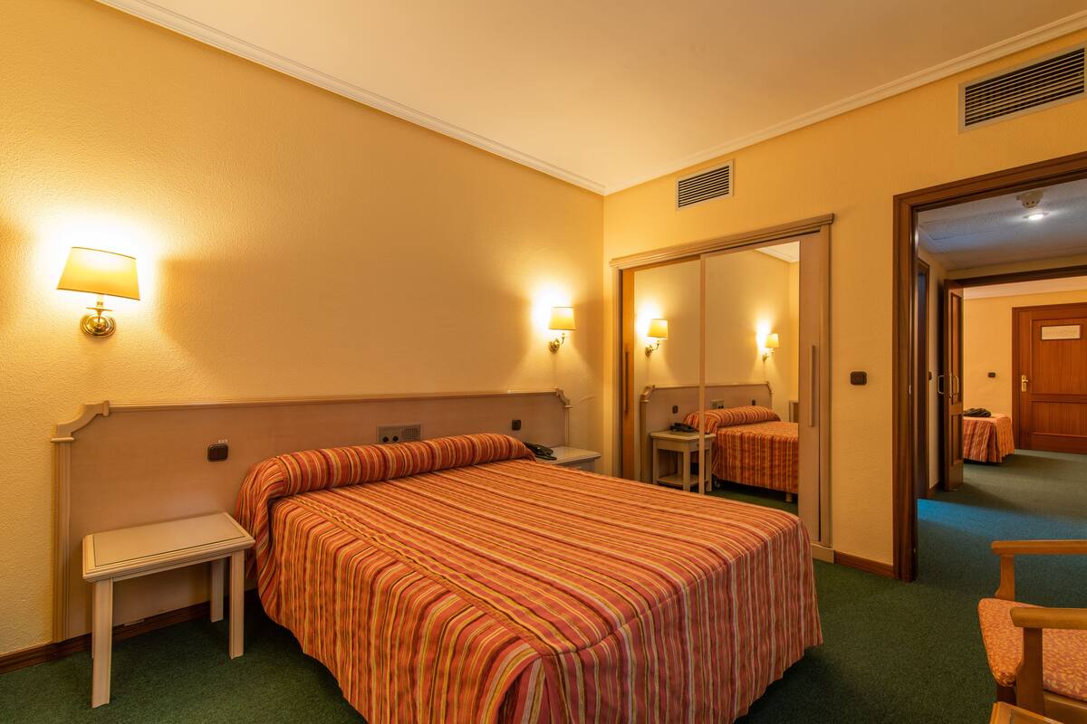 A hotel room with a large bed, bedside tables, a mirror, and a door leading to another room.