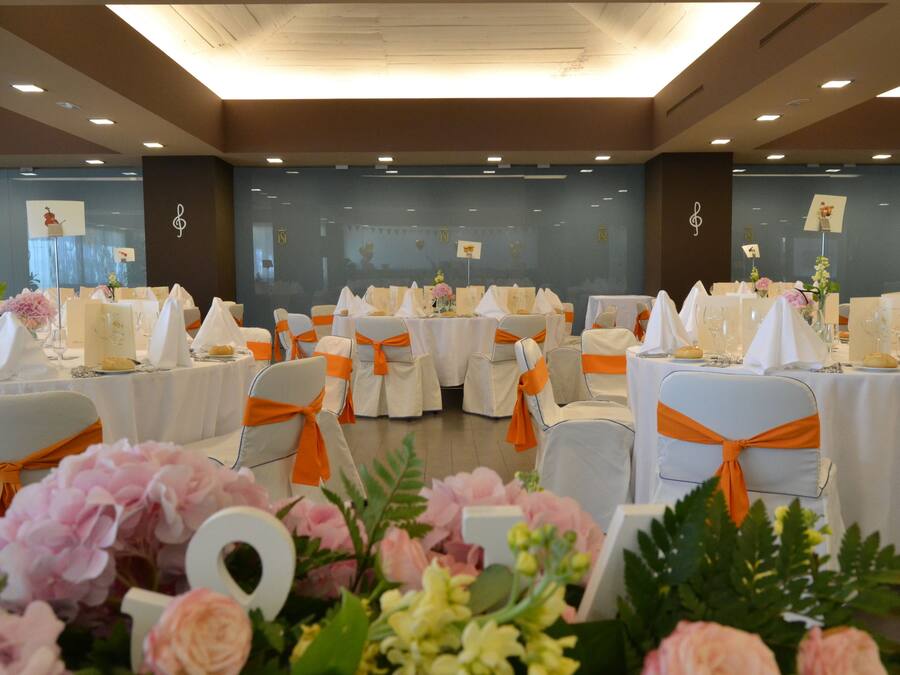 A banquet hall with round tables, white tablecloths, and orange sashes.