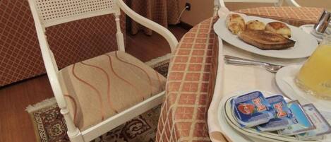 A dining area with a table set for breakfast, including croissants, a plate of food, and a glass of juice. There are two white chairs with patterned cushions.