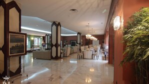 Un hall de hotel espacioso con suelo de mármol, una recepción, zonas de estar y una gran planta en maceta.