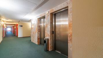 A hallway with two elevators, a trash can, and a sign indicating the direction to the lobby.