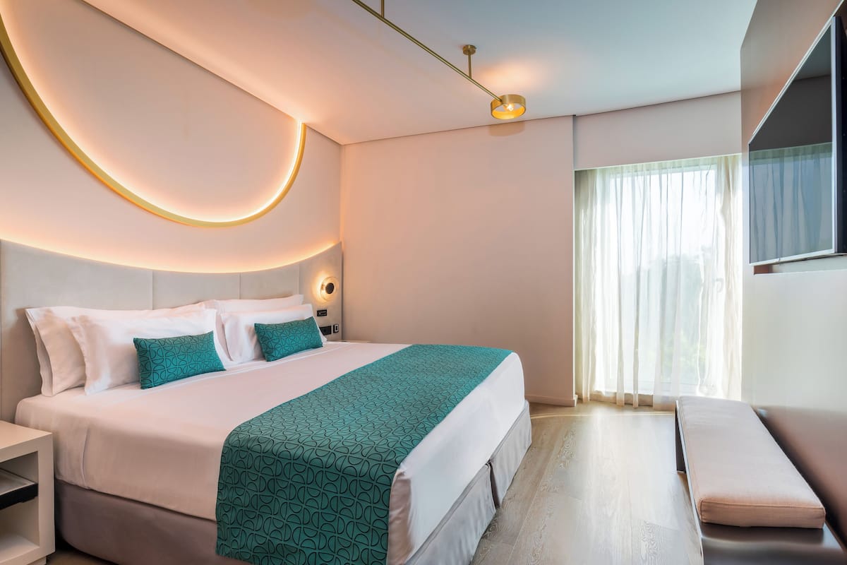 A modern hotel room with a neatly made bed, a bench, and a large window with curtains.