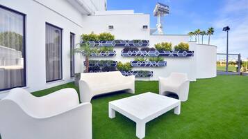 A modern outdoor seating area with white furniture, a white table, and a geometric wall design.