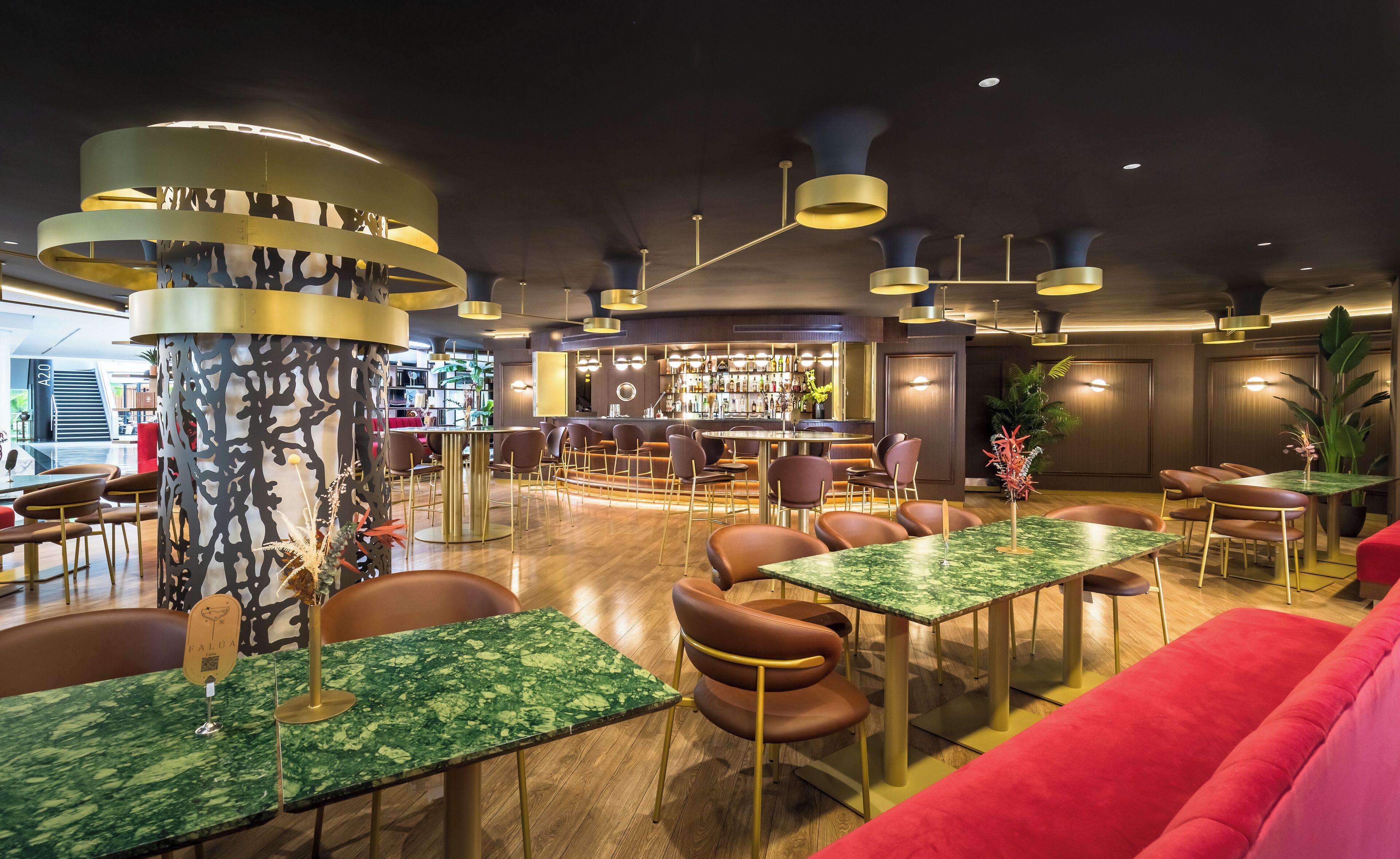 Een moderne bar met een ronde bar, zitplaatsen met ronde tafels en stoelen, en verschillende planten en decoratieve elementen.
