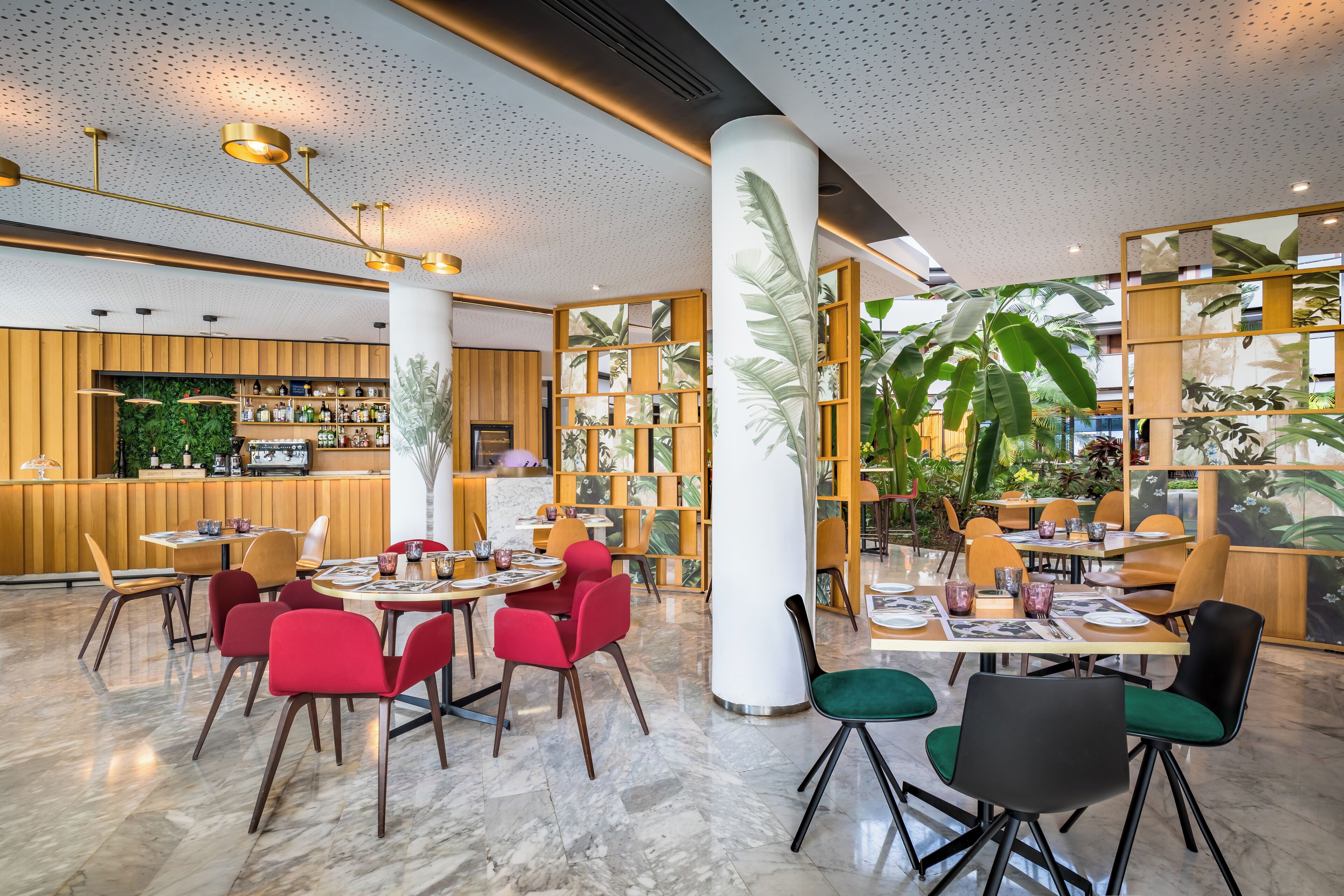 Un restaurant moderne avec un sol en marbre, des chaises rouges et vertes, et un coin bar doté de meubles en bois et de plantes.