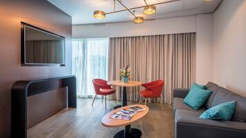 Una sala de estar moderna con un sofá, dos sillones rojos, una mesita de centro y un televisor instalado en la pared.