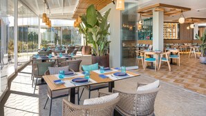 Un restaurante con terraza, amplios ventanales y lámparas colgantes.